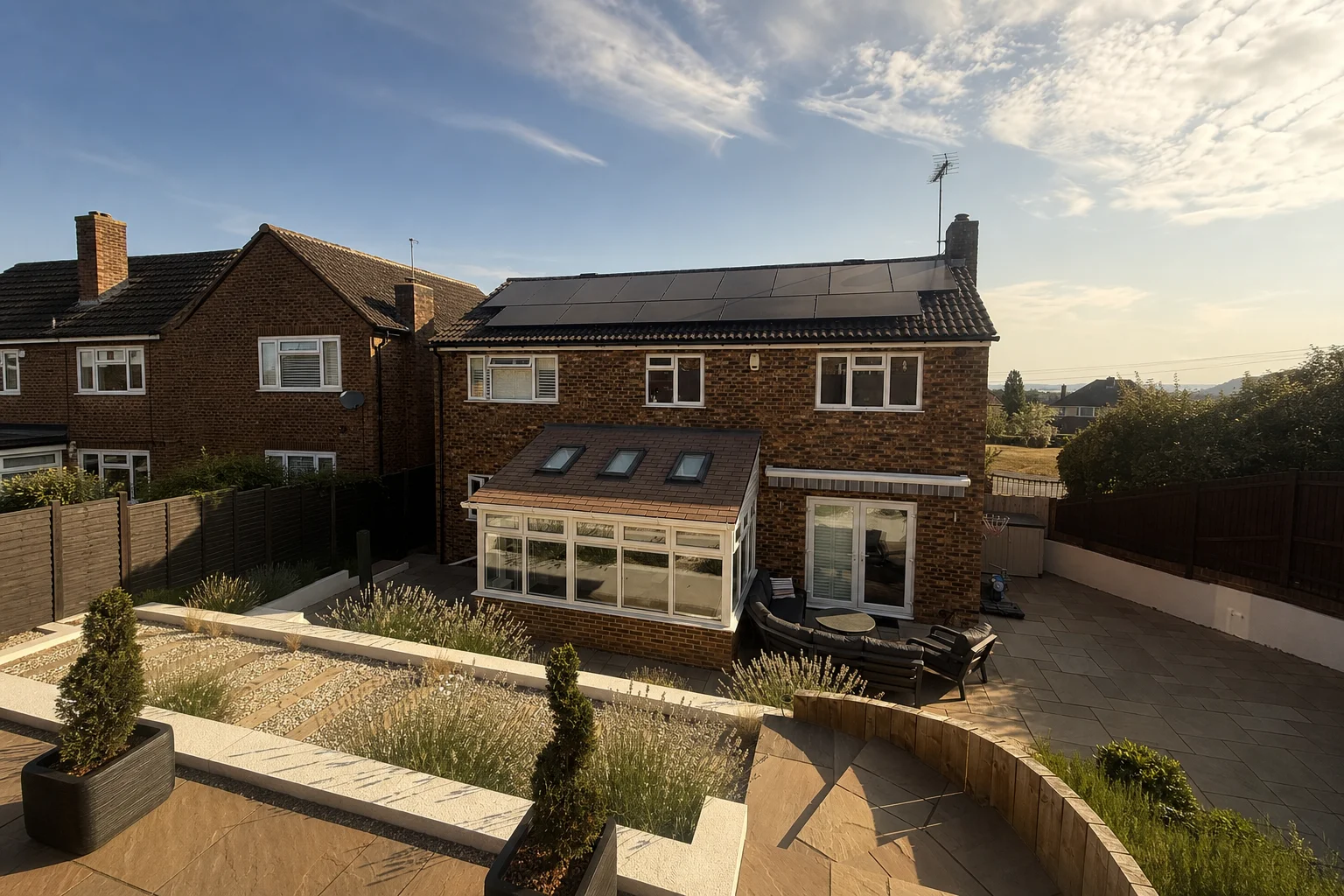 Rear of a brick family home with black solar panels across the roof, at golden hour