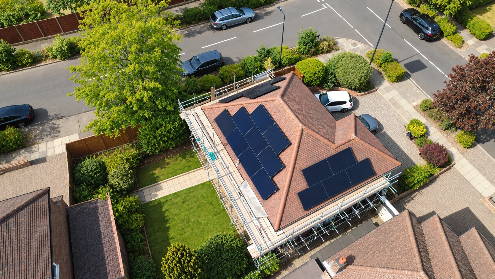 Drone view of black solar panels on a hipped tiled roof, with scaffolding still up on a residential street