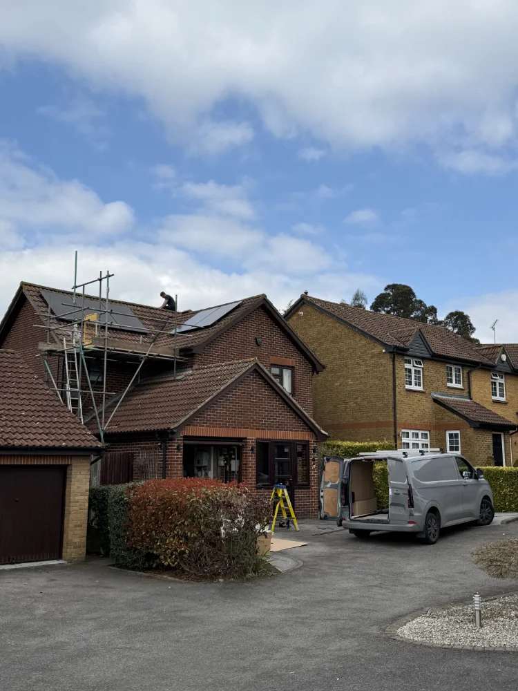 Installer fitting solar panels on a detached house roof with scaffold up