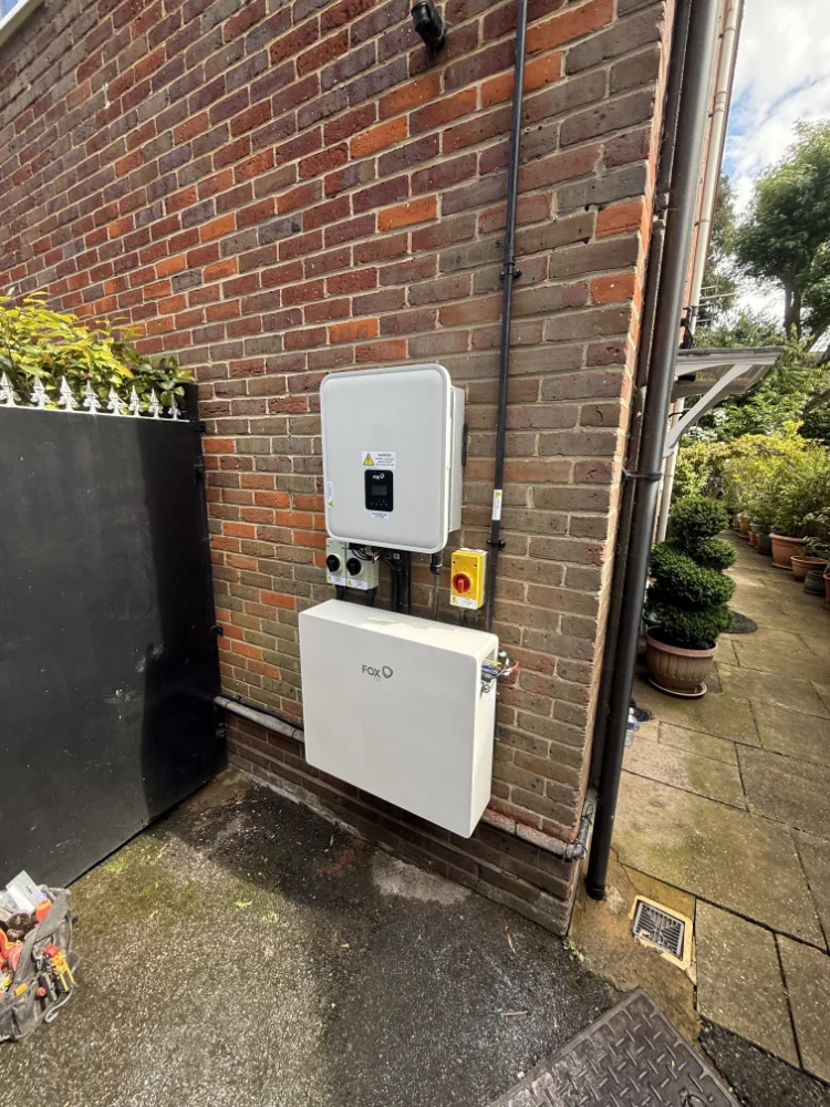 Solar inverter and battery unit mounted on an exterior brick wall next to a patio